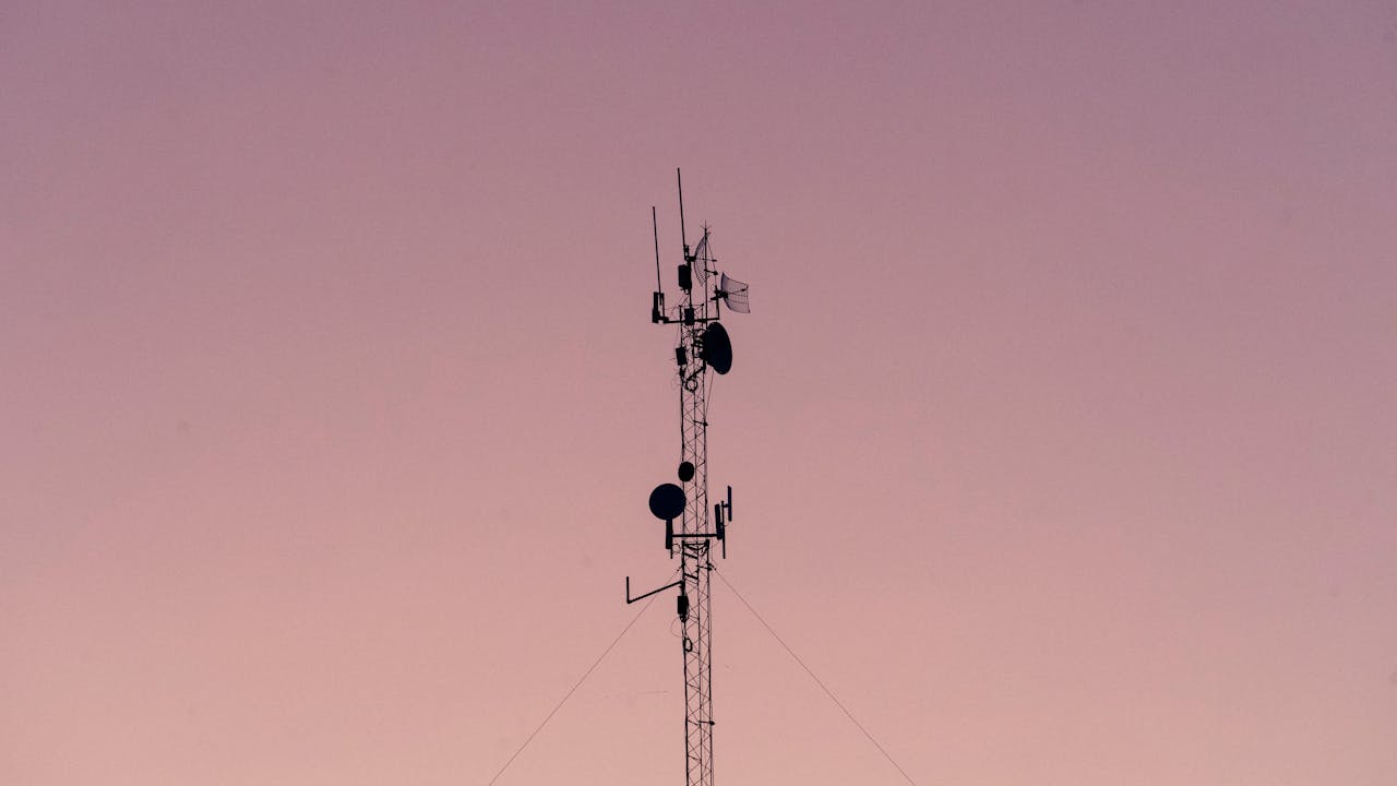 A tall telecommunication tower silhouetted against a clear dusk sky.