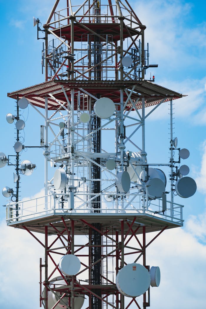 Close-up of a communication tower with antennas and satellite dishes against a blue sky.