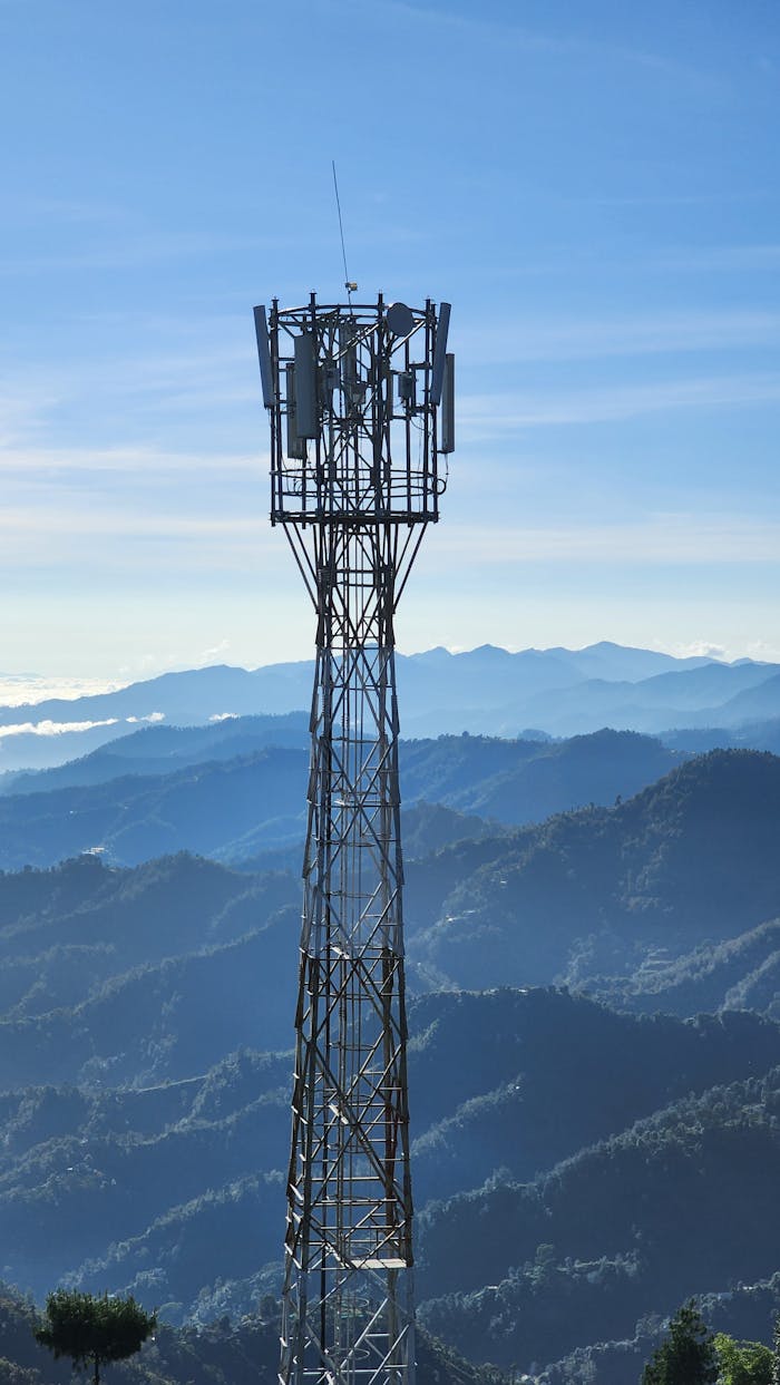 A cell tower stands tall against a panoramic mountain view under a clear blue sky.