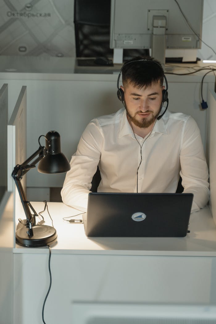 Young professional wearing a headset working on a laptop in a modern office setting.